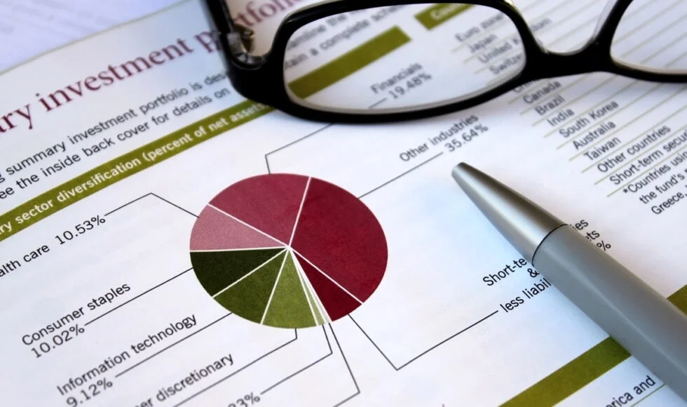 Financial report showing an investment portfolio diversification pie chart with a pen and glasses resting on top.